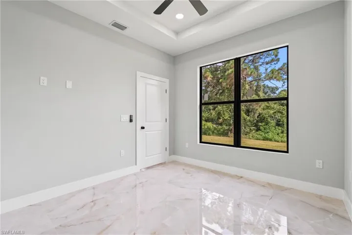 Empty room with light marble finish flooring, a tray ceiling, a ceiling fan, and recessed lighting