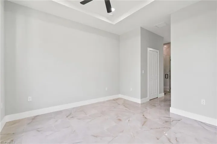 Empty room with light marble finish floors, a raised ceiling, and ceiling fan