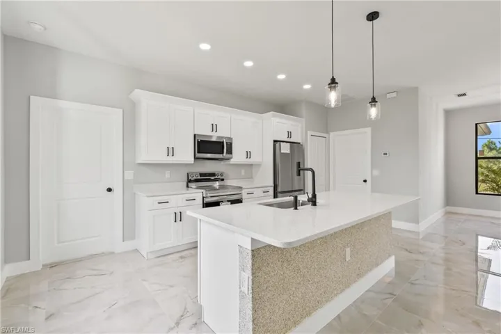 Kitchen featuring light marble finish flooring, an island with sink, appliances with stainless steel finishes, recessed lighting, and white cabinets