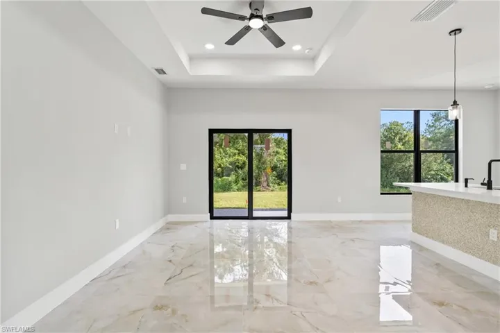 Empty room with plenty of natural light, light marble finish flooring, ceiling fan, a tray ceiling, and recessed lighting