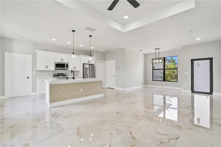 Kitchen with appliances with stainless steel finishes, a kitchen island with sink, white cabinetry, light marble finish floors, and recessed lighting