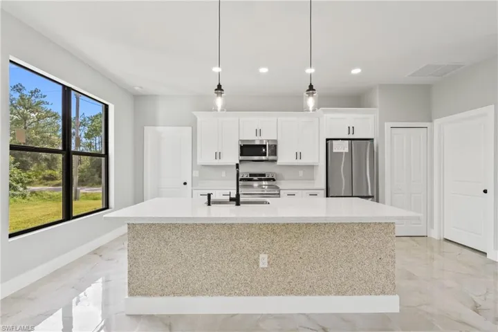 Kitchen with stainless steel appliances, an island with sink, light marble finish floors, white cabinetry, and recessed lighting