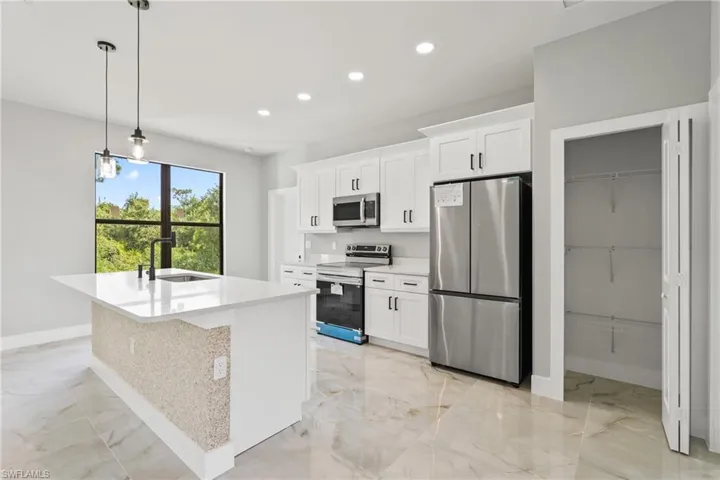 Kitchen with appliances with stainless steel finishes, light marble finish floors, recessed lighting, a kitchen island with sink, and white cabinets