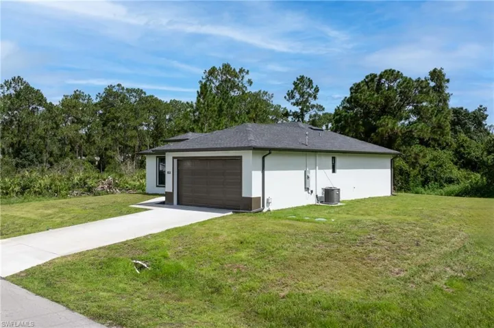 View of side of home featuring a yard, an attached garage, driveway, and stucco siding