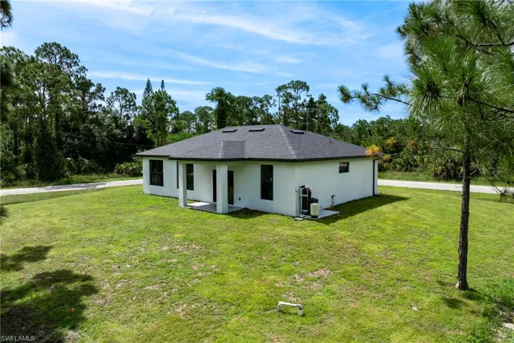 Back of property featuring stucco siding, a yard, roof with shingles, and view of scattered trees