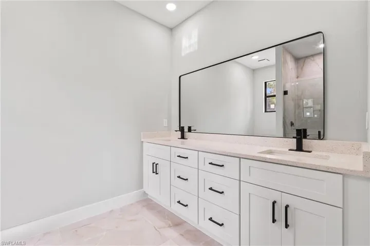 Bathroom featuring a shower stall, double vanity, recessed lighting, and marble finish flooring