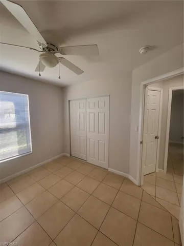 Unfurnished bedroom with a closet, light tile patterned flooring, and a ceiling fan