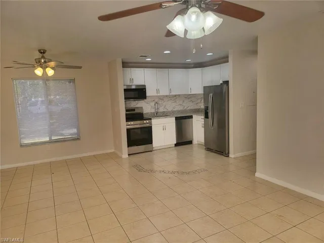 Kitchen featuring a ceiling fan, white cabinetry, stainless steel appliances, light tile patterned floors, and backsplash