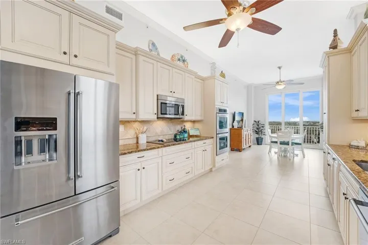 The remodeled kitchen is thoughtfully designed with stainless steel appliances, custom cream wood cabinetry accented by under-cabinet and uplighting, granite countertops, and a beautifully textured tumbled marble backsplash.