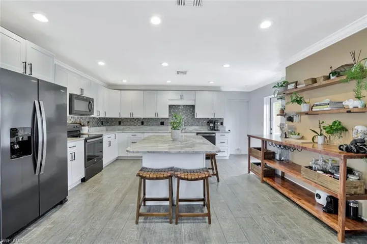 Kitchen with light wood-type flooring, white cabinets, range with electric cooktop, stainless steel refrigerator with ice dispenser, and tasteful backsplash