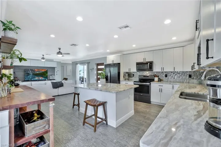 Kitchen featuring light hardwood / wood-style flooring, a kitchen island, ceiling fan, light stone countertops, and appliances with stainless steel finishes