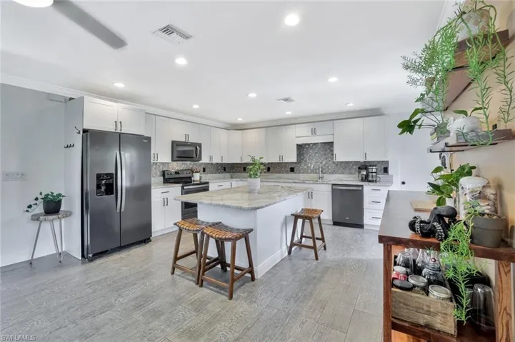 Kitchen featuring light hardwood / wood-style flooring, stainless steel appliances, tasteful backsplash, a center island, and white cabinets