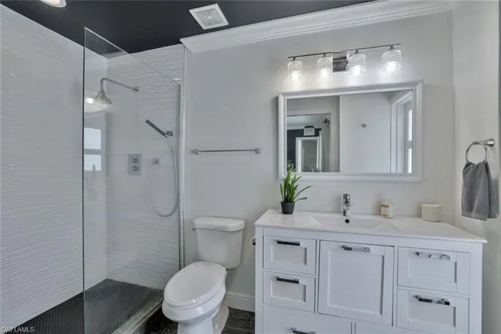 Bathroom featuring oversized vanity, ornamental molding, toilet, and a shower with door