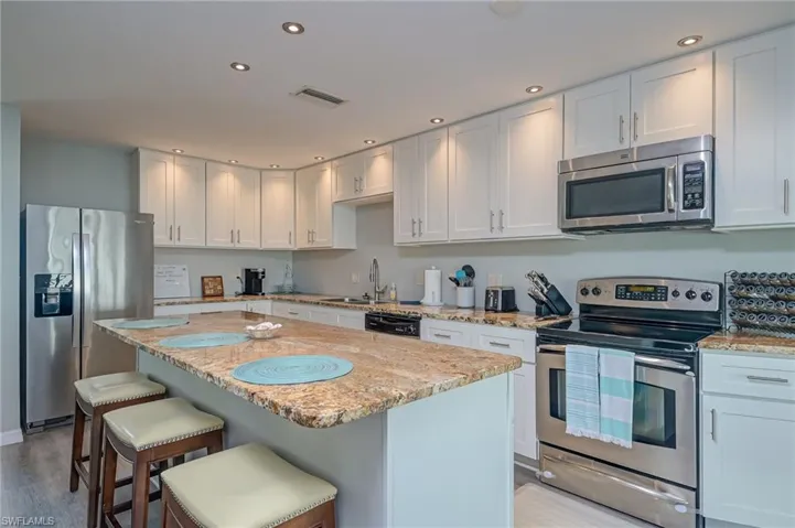 Kitchen featuring stainless steel appliances, white cabinets, a center island, light stone counters, and a breakfast bar area