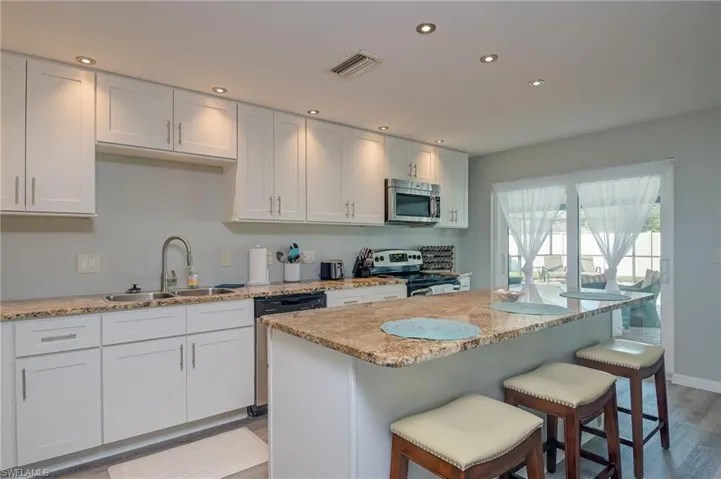 Kitchen with recessed lighting, light stone countertops, stainless steel appliances, white cabinets, and light wood-style floors