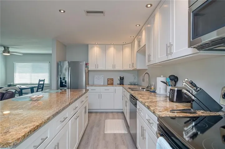 Kitchen featuring stainless steel appliances, white cabinetry, recessed lighting, light stone countertops, and light wood-style flooring