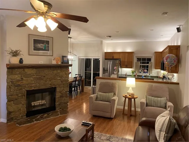 Living area with a ceiling fan, wood finished floors, and a stone fireplace