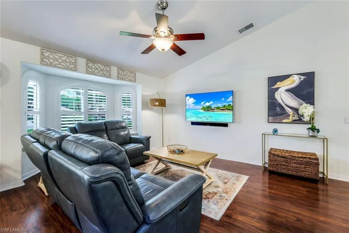 Living room with dark wood-type flooring, ceiling fan, and vaulted ceiling