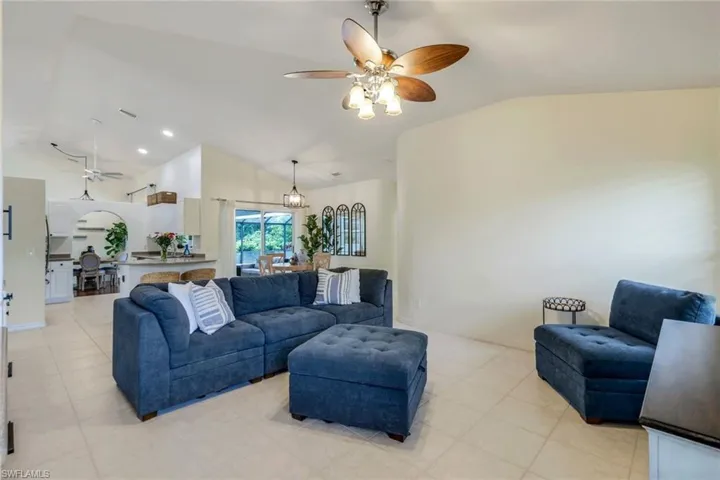 Living room featuring light tile flooring, ceiling fan with notable chandelier, and lofted ceiling