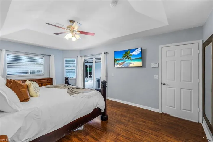 Bedroom featuring ceiling fan, access to exterior, dark hardwood / wood-style flooring, and a tray ceiling