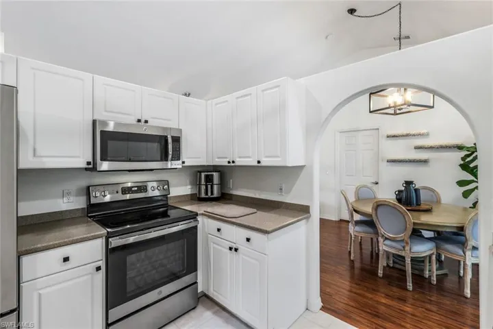 Kitchen with appliances with stainless steel finishes, white cabinets, light wood-type flooring, and an inviting chandelier