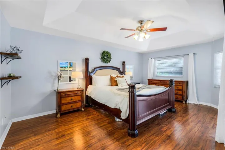 Bedroom featuring dark hardwood / wood-style flooring, ceiling fan, and a raised ceiling