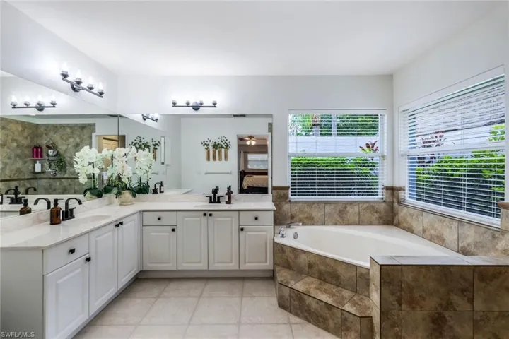 Bathroom featuring tile floors, dual vanity, and tiled bath