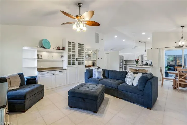 Living room featuring high vaulted ceiling, ceiling fan with notable chandelier, and light tile flooring