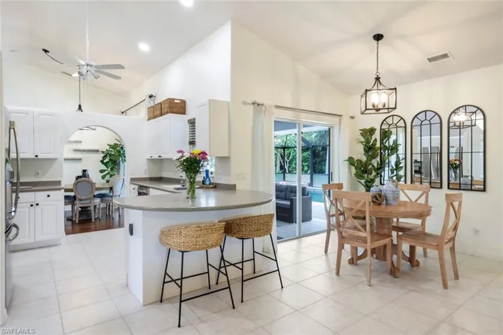 Kitchen featuring white cabinets, a breakfast bar area, light tile floors, and ceiling fan with notable chandelier