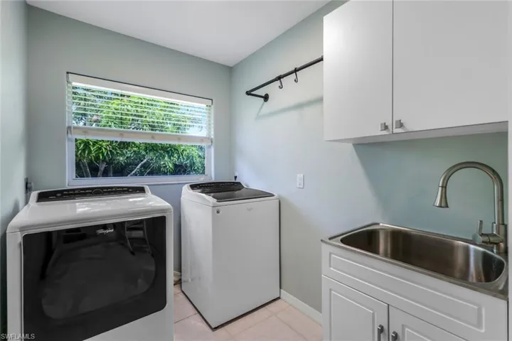 Laundry room with light tile floors, sink, cabinets, and separate washer and dryer