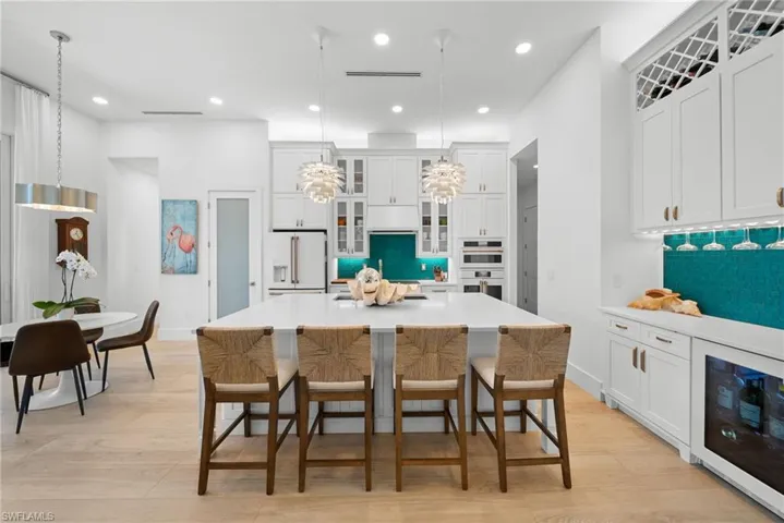 Kitchen featuring glass fronted cabinets, wine cooler, pendant lighting, light wood-style floors, and white cabinetry