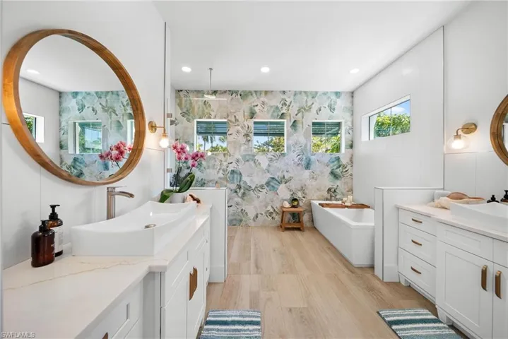 Bathroom with two vanities, a freestanding bath, recessed lighting, and light wood-style floors
