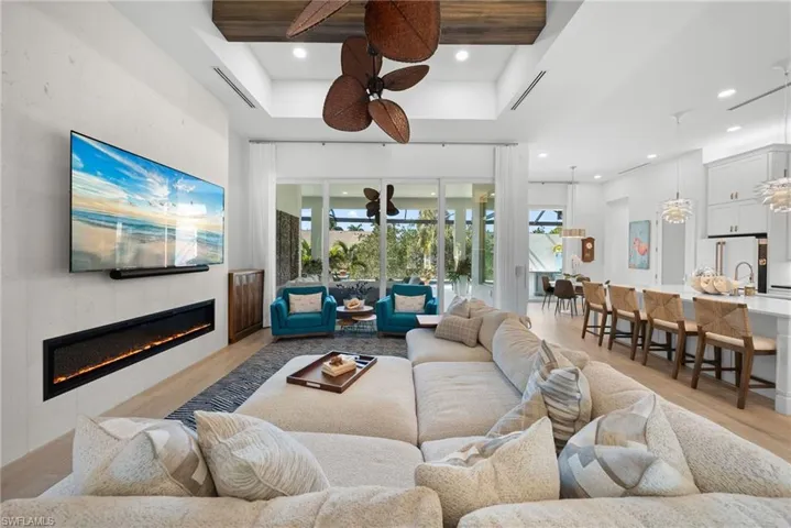 Living room featuring light wood-type flooring, a tiled fireplace, a high ceiling, a ceiling fan, and recessed lighting