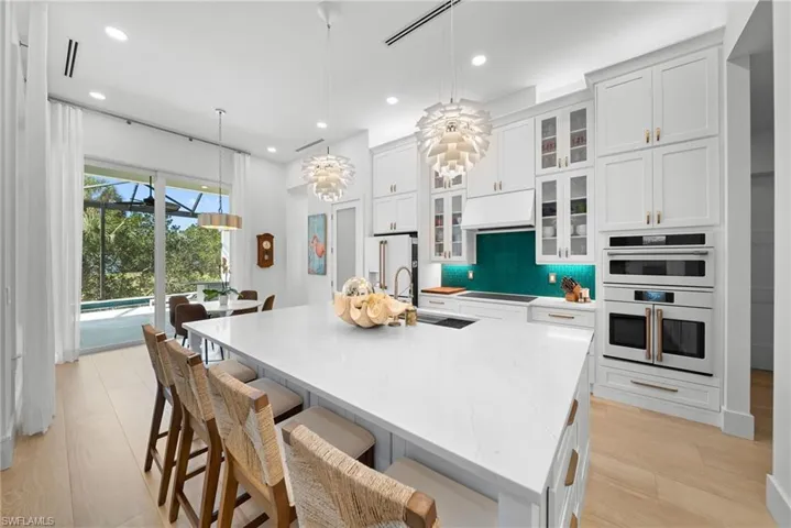 Kitchen with glass insert cabinets, white cabinetry, hanging light fixtures, light stone counters, and a breakfast bar