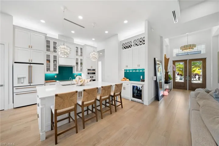 Kitchen featuring glass insert cabinets, high end white fridge, a breakfast bar, suspended lighting, and white cabinets