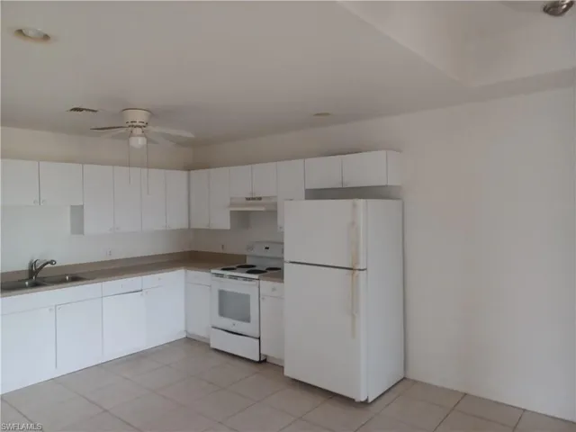 Kitchen with white appliances, a ceiling fan, white cabinetry, under cabinet range hood, and light countertops