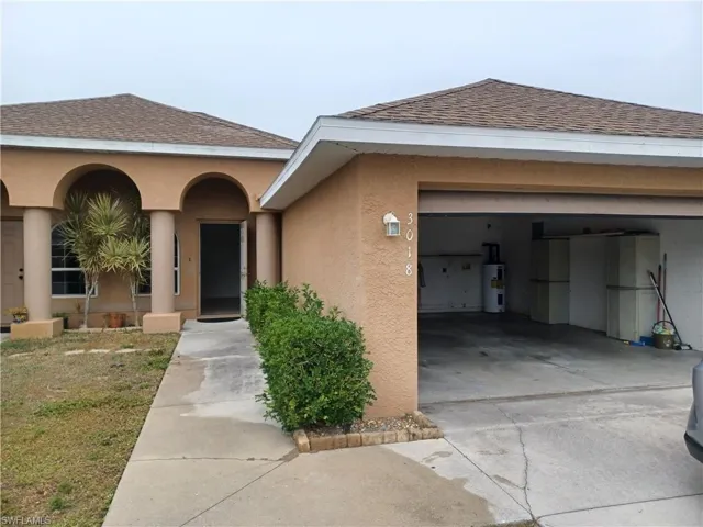 View of front facade featuring roof with shingles, stucco siding, driveway, an attached garage, and water heater