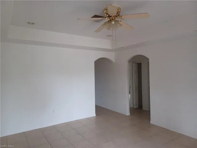 Empty room featuring a raised ceiling, light tile patterned floors, a ceiling fan, and arched walkways