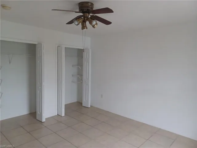 Unfurnished bedroom with two closets, ceiling fan, and light tile patterned floors