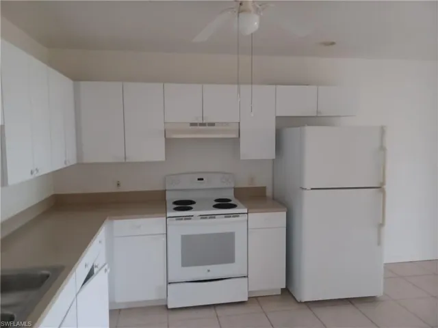 Kitchen with white appliances, white cabinets, under cabinet range hood, and light countertops