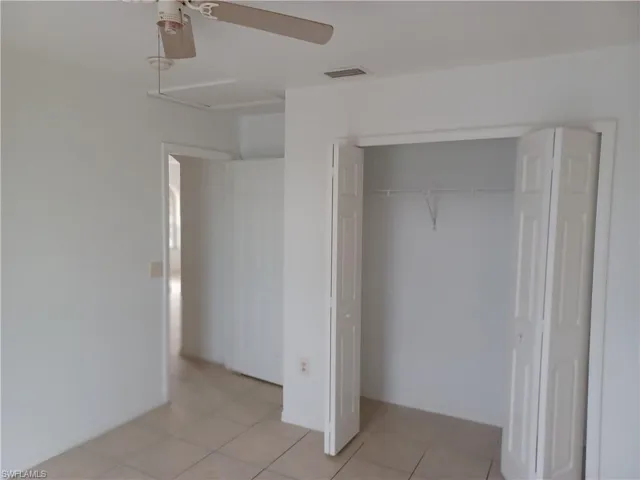 Unfurnished bedroom with light tile patterned floors, ceiling fan, a closet, and attic access
