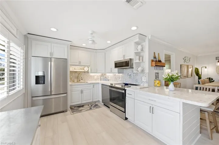 Kitchen with stainless steel appliances, light stone countertops, crown molding, open shelves, and tasteful backsplash