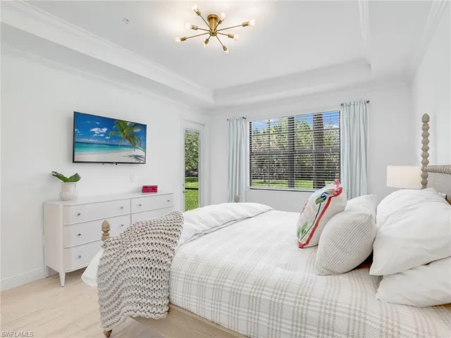 Bedroom with a raised ceiling, light wood-style floors, a chandelier, crown molding, and baseboards