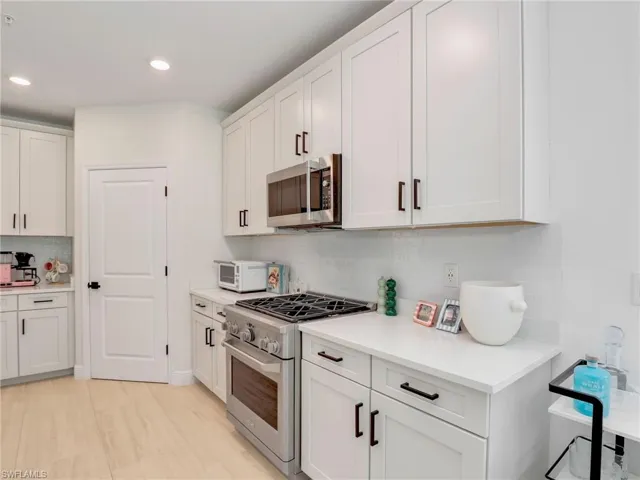 Kitchen with stainless steel appliances, decorative backsplash, light countertops, white cabinetry, and recessed lighting