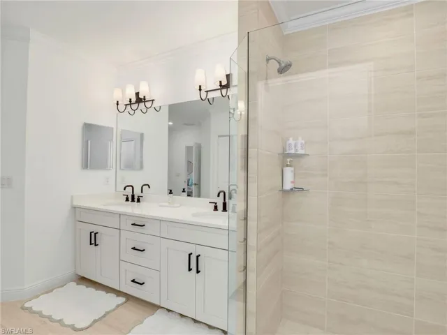 Bathroom featuring double vanity, a shower stall, and crown molding