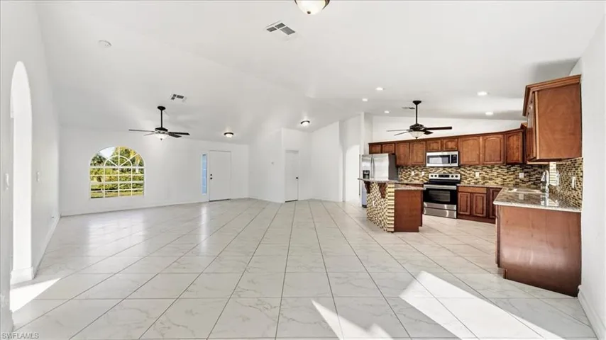 Kitchen featuring backsplash, a kitchen bar, light marble finish floors, appliances with stainless steel finishes, and a kitchen island