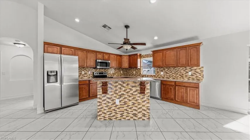Kitchen featuring vaulted ceiling, arched walkways, appliances with stainless steel finishes, light stone countertops, and backsplash