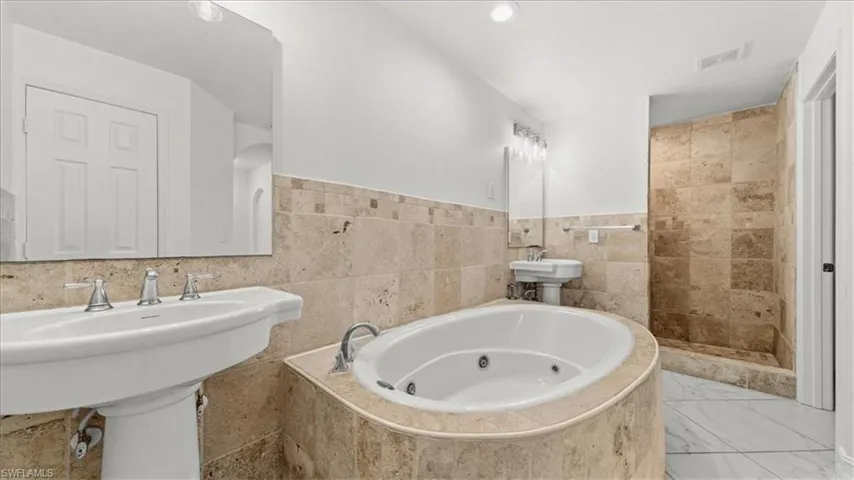 Bathroom with tile walls, a jetted tub, wainscoting, and a stall shower