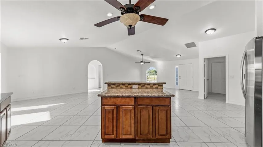 Kitchen with lofted ceiling, arched walkways, freestanding refrigerator, open floor plan, and light marble finish floors