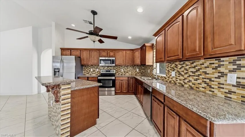 Kitchen featuring lofted ceiling, backsplash, stainless steel appliances, light stone counters, and light marble finish flooring